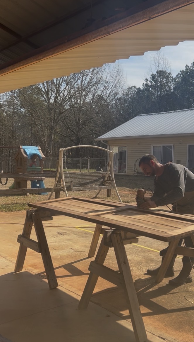Michael Bevis hand-sanding a custom wood door on sawhorses outside the shop