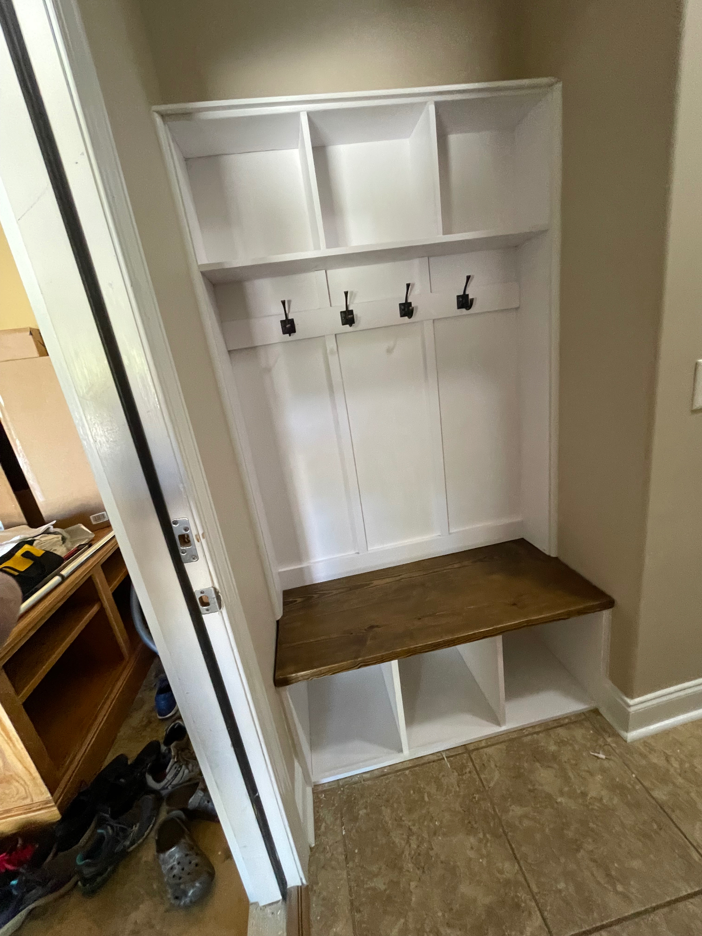 Built-in white mudroom nook with cubbies, hooks and a stained wood bench