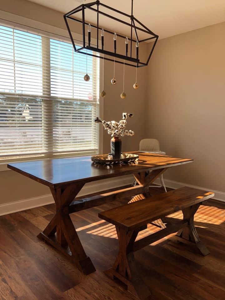 Dark stained X-base farmhouse dining table with matching bench in a sunlit dining room